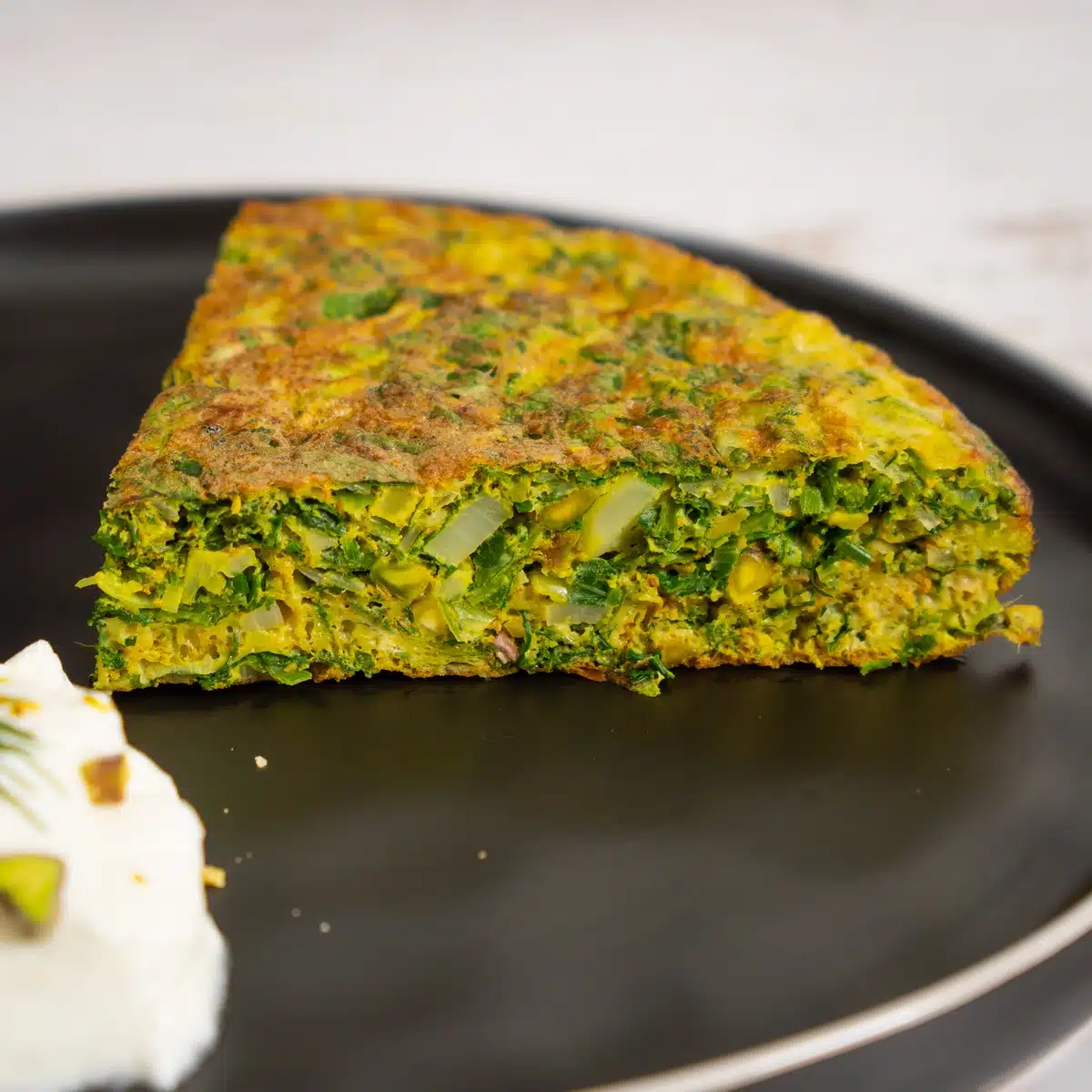 Kuku Sabzi - A healthy Green Frittata Delicious kuku sabzi on a plate with yogurt