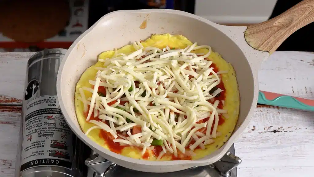 10-Minute Pizza Omelette – The Perfect Cheesy Breakfast add pizza sauce and toppings with cheese on top of egg